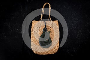 Pounamu fish hook necklace on weaved bag on dark background. Aotearoa, New Zealand, Maori.