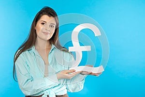 The girl holds a large pound symbol in her hands. Great Britain currency shape. Symbol of finance and cash flow in the