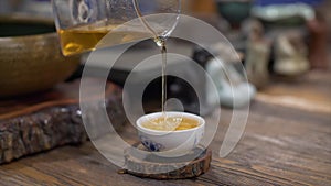 Pour brewed green tea in white ceramic cup from glass teapot slow motion