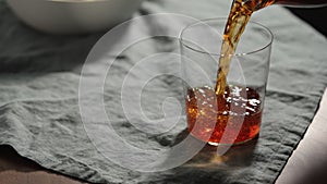 pour chinotto soft drink in tumbler glass on linen cloth