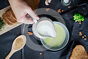 Pour cream into cream soup. Close-up. Milk jug with cream in female hands.