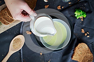 Pour cream into cream soup. Close-up. Milk jug with cream in female hands.