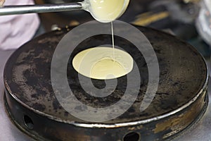 Pour the dough from a ladle of ladles on a hot hot pancake maker. the process of making pancakes, traditional Thai fast food for