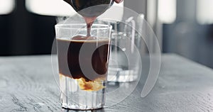 pour espresso into tonic with clear ice cube in tumbler glass on black oak table