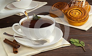 pour hot black tea into a white cup. aromatic tea with sugar and mint. delicious cinnamon rolls for breakfast.