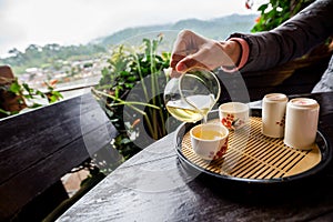 Pour the hot tea into a cup on wooden table with mountain view