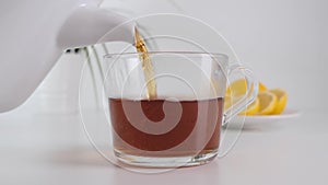 Pour hot tea on glass cup. White teapot. Slow motion.