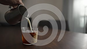 pour milk into cold brew coffee over ice ball in tumbler glass on walnut table