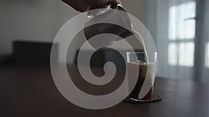 pour milk over cold brew coffee over ice cube in tumbler glass on walnut table