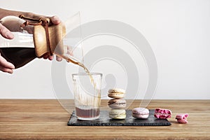 Pour over coffee brewing method Chemex, woman hands hold a glass bowl, still life with brownie cookies on wooden table.