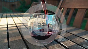 Pour red wine into stemless glass on a wood table outside in the evening