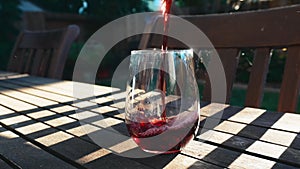 Pour red wine into stemless glass on a wood table outside in the evening