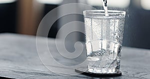 pour tonic water over clear ice ball in tumbler glass on black oak table