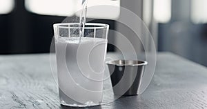 pour tonic water over clear ice ball in tumbler glass on black oak table