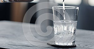 pour tonic water over clear ice ball in tumbler glass on black oak table