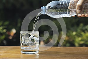 Pour water into a glass on wooden table in nature background