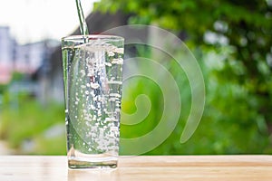 Pour water into glass on wooden table outdoors and green background