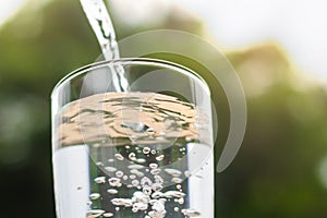 Pour water into glass on wooden table outdoors and green background