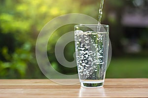 Pour water into glass on wooden table outdoors and green background