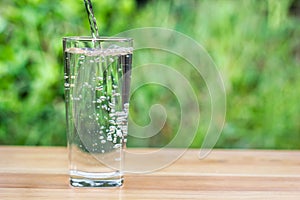 Pour water into glass on wooden table outdoors and green background