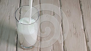 Pour yogurt into glass on vintage wooden boards top view. Milk drink in a transparent glass