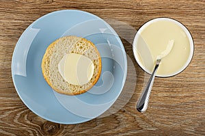 Poured condensed milk bun in blue plate, spoon in bowl with condensed milk on wooden table. Top view