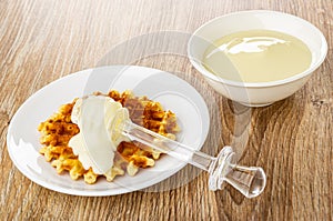 Poured condensed milk, transparent dipper on wafer in saucer, bowl with condensed milk on table