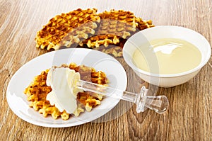 Poured condensed milk, transparent dipper on wafer in saucer, wafers, bowl with condensed milk on table