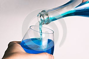Pouring alcohol from a bottle into a glass goblet on a white background. Glass of wine and a bottle with pouring liquid