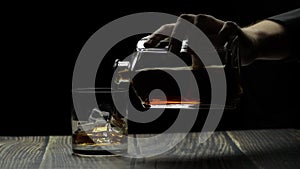 Pouring alcohol drink whiskey, cognac into glass. Black background. Silhouettes