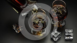 Pouring alcohol drink whiskey, cognac into glass with ice cubes. Slow motion