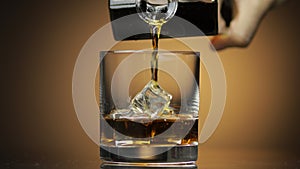 Pouring alcohol drink whiskey, cognac into glass with ice. Dark background.