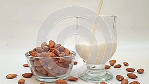 Pouring almond milk in a glass in a white background with a bowl of almonds beside. Pouring non dairy nut milk in glass.