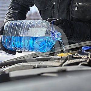 Pouring an antifreeze liquid in a windshield washer tank of a car close up