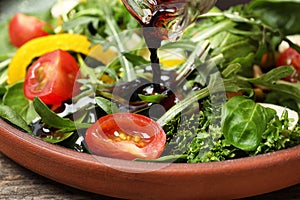 Pouring balsamic vinegar to fresh vegetable salad on plate