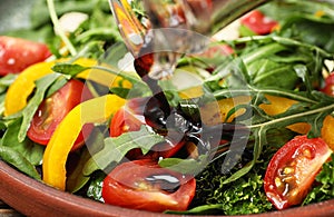 Pouring balsamic vinegar to fresh vegetable salad on plate