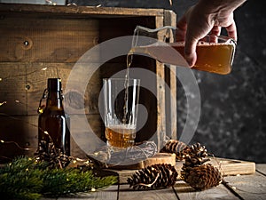 Pouring beer into a tall glass on wooden background with christmas lights