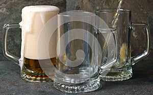 Pouring beer into traditional beer steins on black slate background.