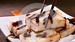 Pouring black soy sauce on ready-to-eat delicious turnip cake, Chinese traditional local dish radish cake in restaurant, close up