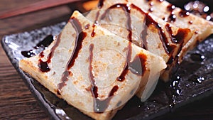 Pouring black soy sauce on ready-to-eat delicious turnip cake, Chinese traditional local dish radish cake in restaurant, close up