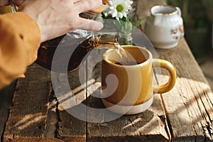 Pouring black tea from teapot into ceramic mug.