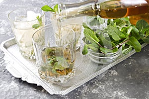 Pouring bourbon into a glass, process of making mint julep.Closeup of an old-fashioned glass with mint and crushed ice on the silv