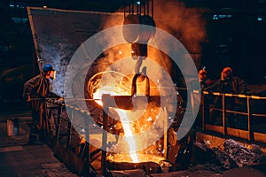 Pouring bright liquid iron or metal with sparks into container in steel mill or workshop blast furnace foundry. Metal