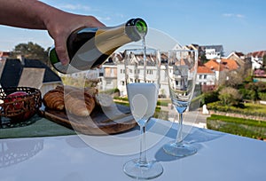 Pouring of brut champagne sparkling wine in flute glasses on outdoor terrace in France