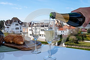 Pouring of brut champagne sparkling wine in flute glasses on outdoor terrace in France