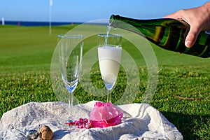 Pouring of bubbles white champagne or cava wine during romantic event or celebration on green golf club grass with sea view