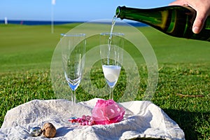 Pouring of bubbles white champagne or cava wine during romantic event or celebration on green golf club grass with sea view