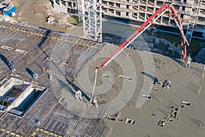 Pouring cement on the floors of residential multi-story building under construction using a concrete pump truck with high boom to