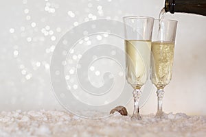 Pouring champagne from bottle into glass on snow with bokeh background with copy space