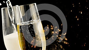 Pouring champagne into flutes with gold bubbles with golden abstract glitter sparkle lights fireworks on black background